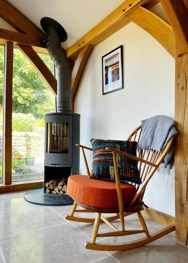 a cosy timber framed cabin showing curved braces a woodburner and a rocking chair